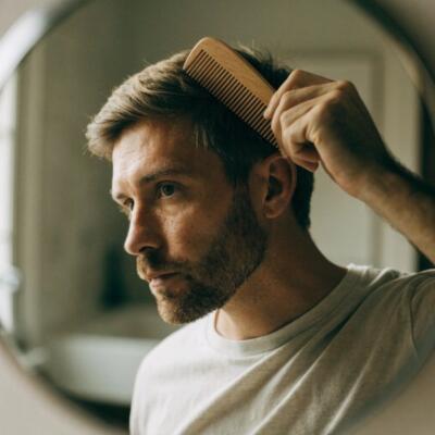 Homme qui se coiffe les cheveux avec un peigne en bois : soin cheveux homme