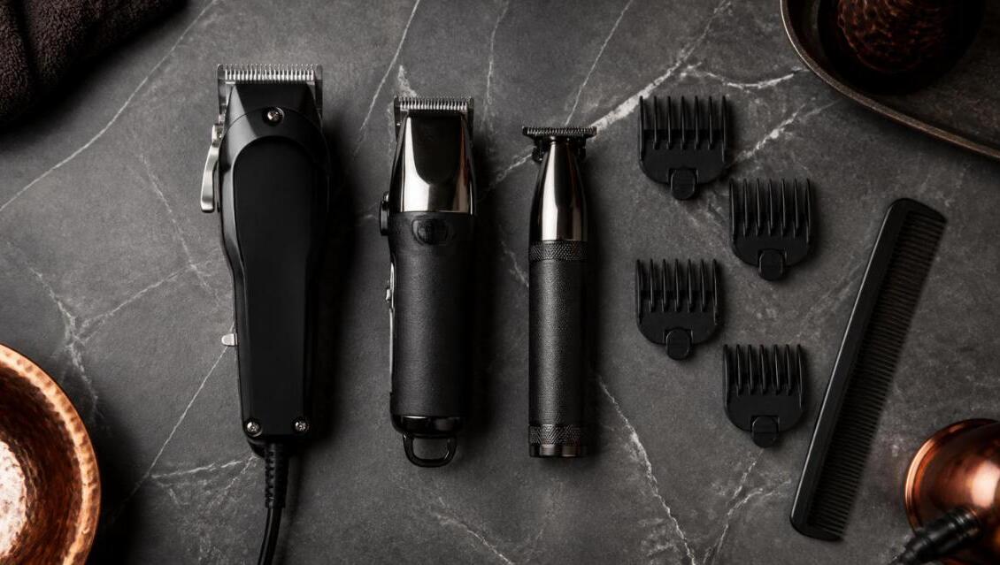 Trois tondeuses à cheveux électriques noires avec sabots de coupe et peigne, posés sur un plan de travail en marbre